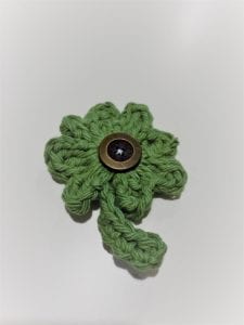 Finished crochet four leaf clover in green yarn with brown button at center.