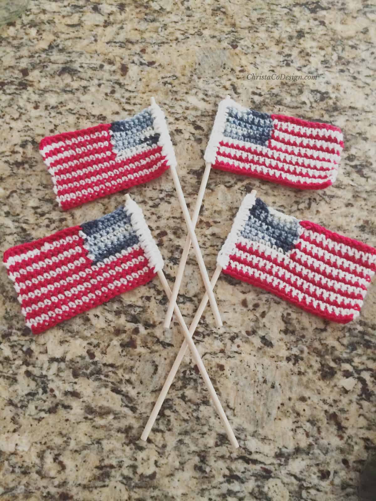 4 crochet American flags with dowels crossed at center on counter.