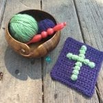 Purple prayer cloth with crochet cross in green on deck with yarn bowl and hook.