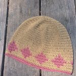 Pink and brown crochet beanie laid on wood deck.