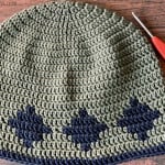 Green crochet hat with blue diamonds on wood table.