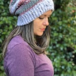 Woman in striped slouchy hat in pink and grey looking down.