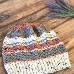 Striped slouchy hat in white, grey and pink laid flat with lavender.