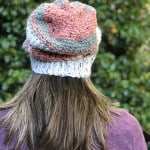 Back view of woman in crochet slouchy hat in pink, grey and white.