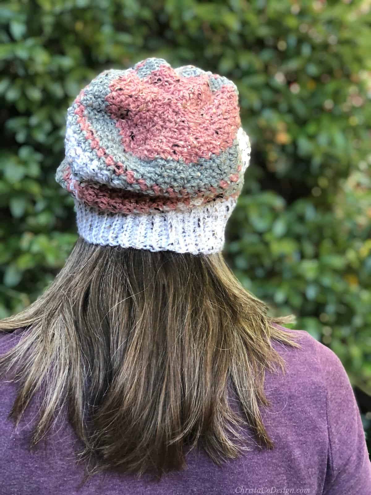 Back view of woman in crochet slouchy hat in pink, grey and white.