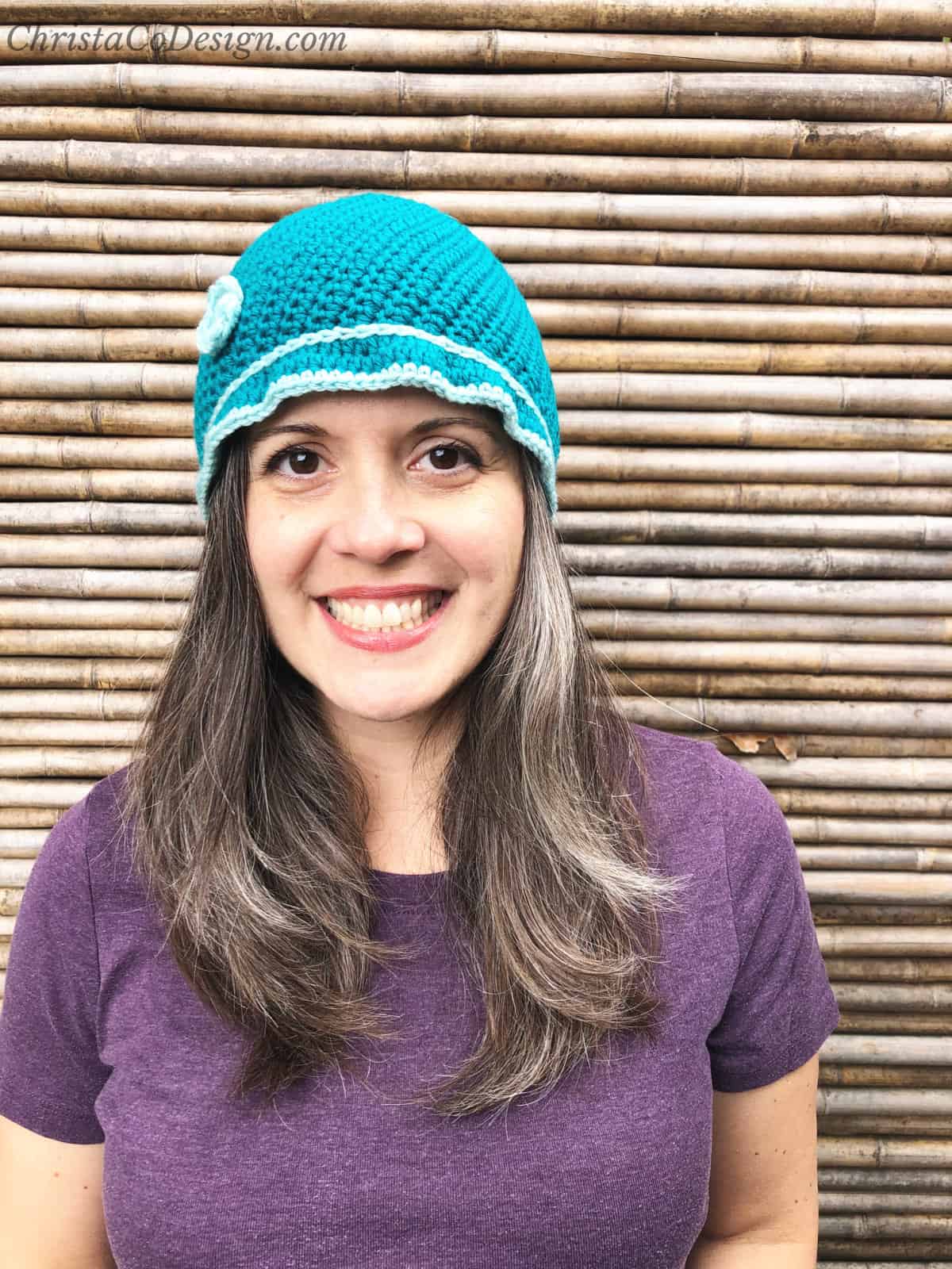 Woman smiling with crochet cloche hat in blue over long brown hair.