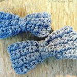 Two grey crochet bowties on wood table.