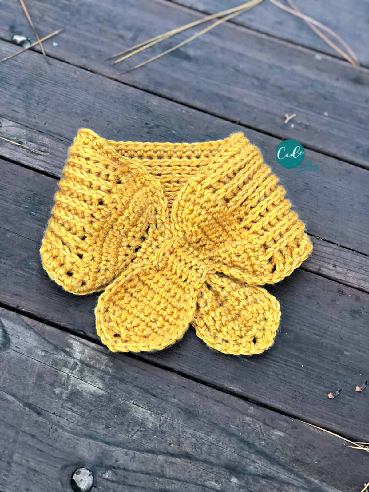 Crochet scarflette in yellow crossed and flat on boards.