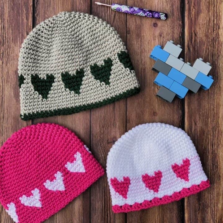 Three sweetheart hats in various colors laid by Lego heart.