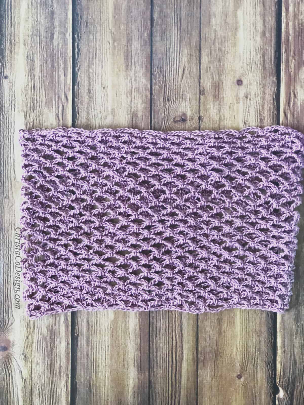 Lilac crochet cotton cowl pattern laid flat on wood back drop.