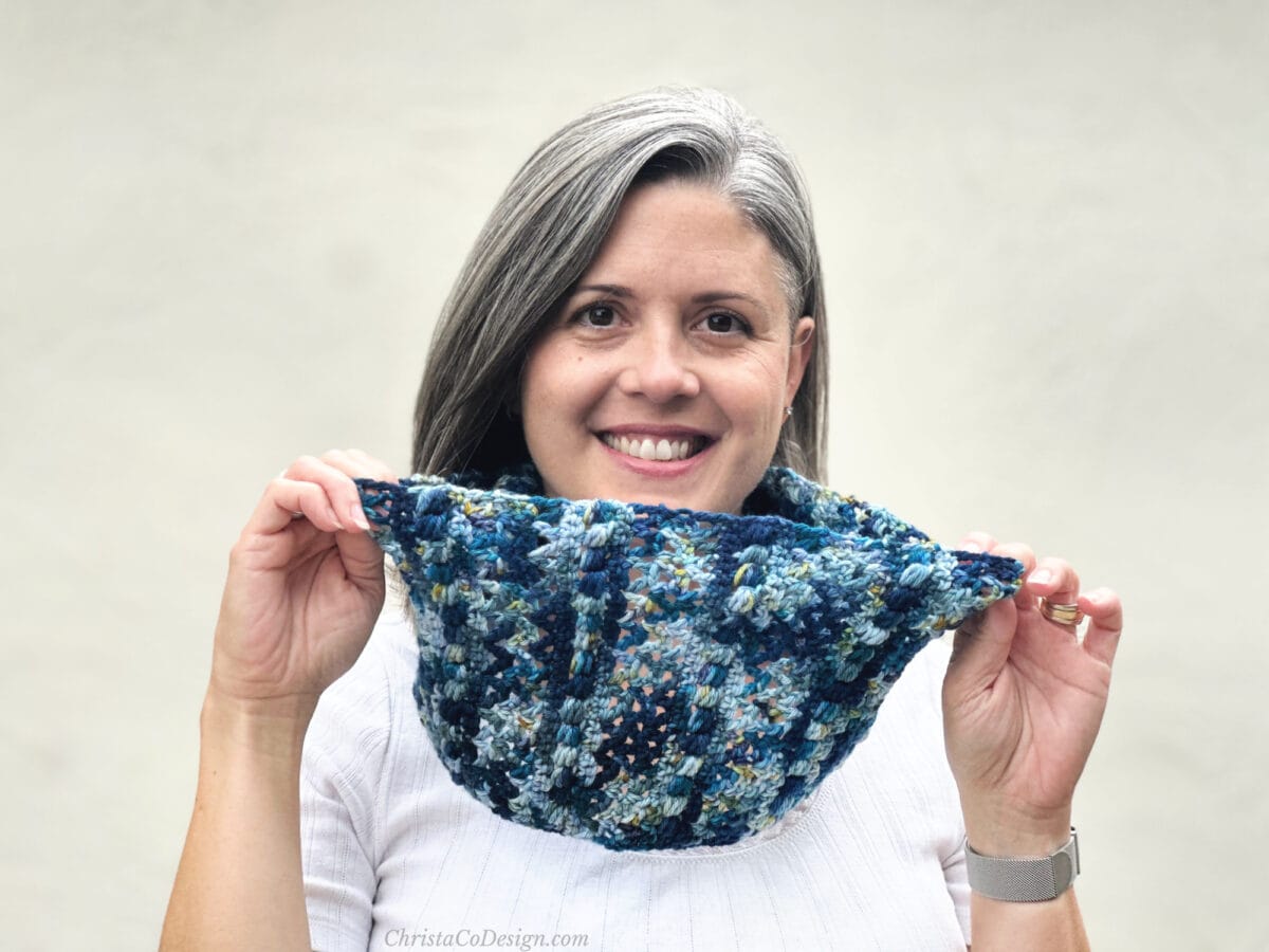 Woman in blue crochet cowl smiling.