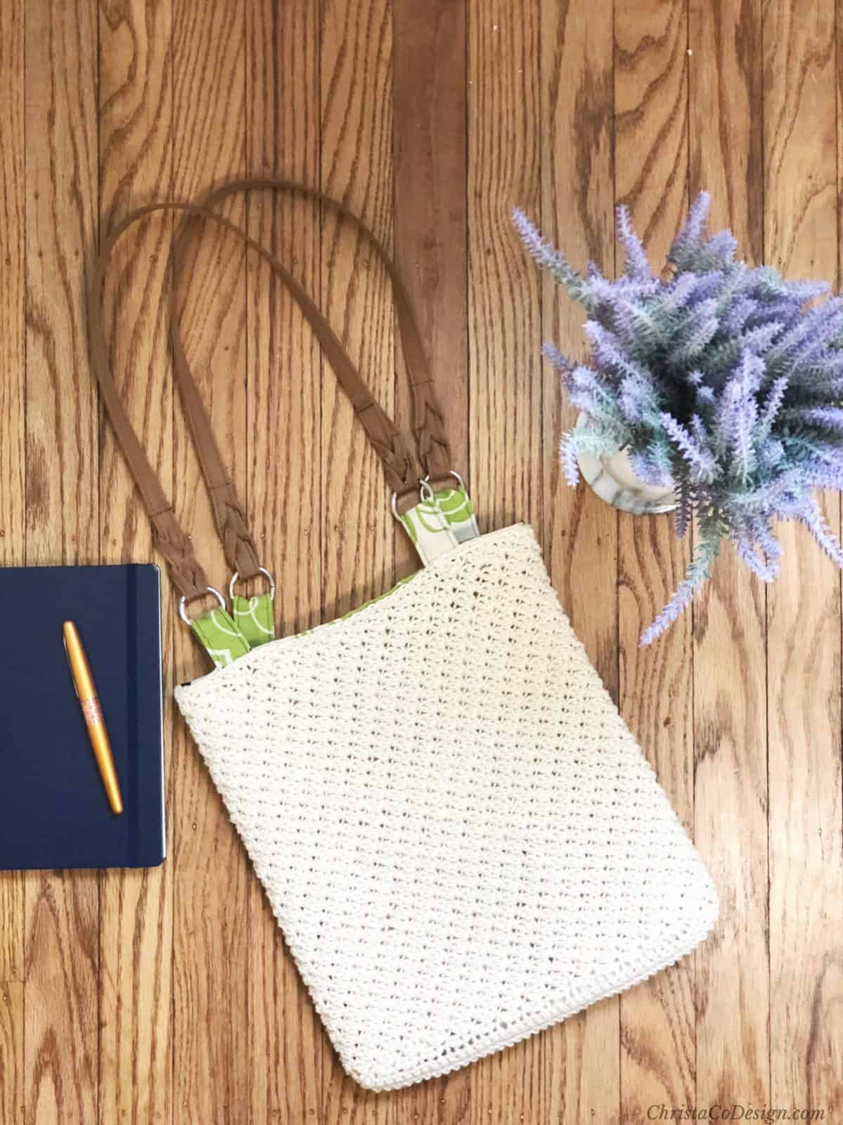 Crochet bag with green lining flat on wood floor.