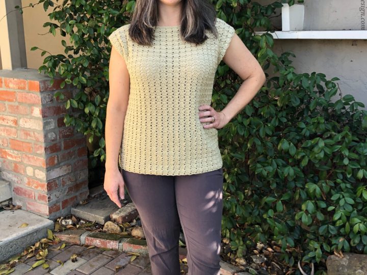 Woman outside in front of vine wearing beige crochet top.