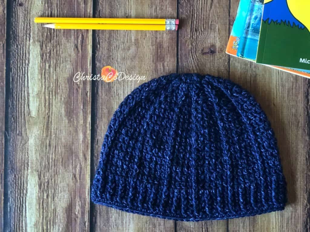 Blue crochet hat pattern in ribbing with pencil and books.