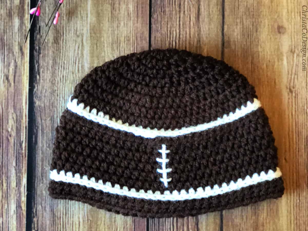 Brown crochet beanie with white stitching like football.