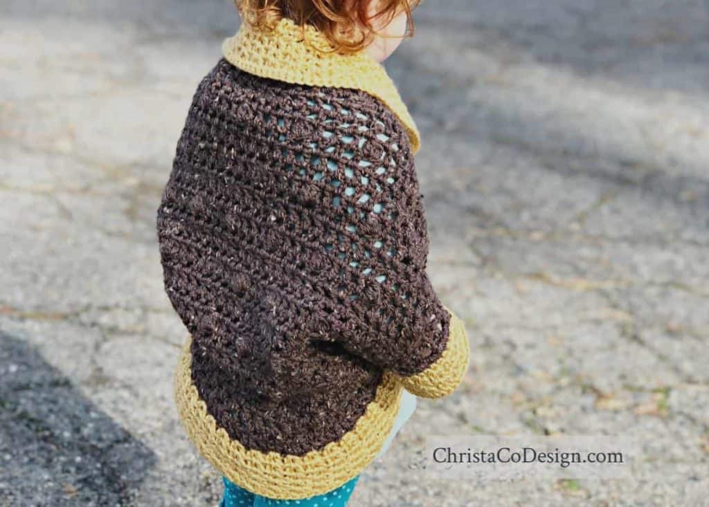 Toddler in brown sweater with gold trimmed sleeves.