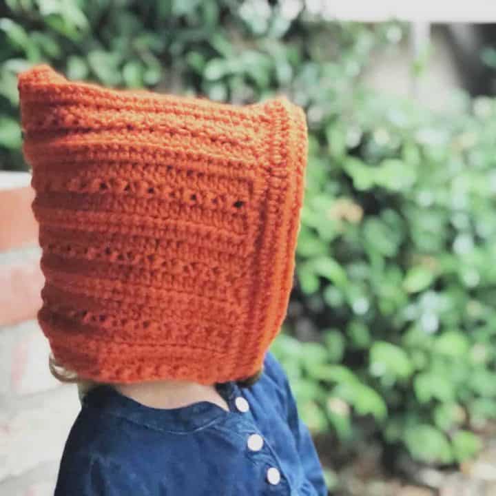 Toddler in rust colored crochet pixie hat pattern outside.