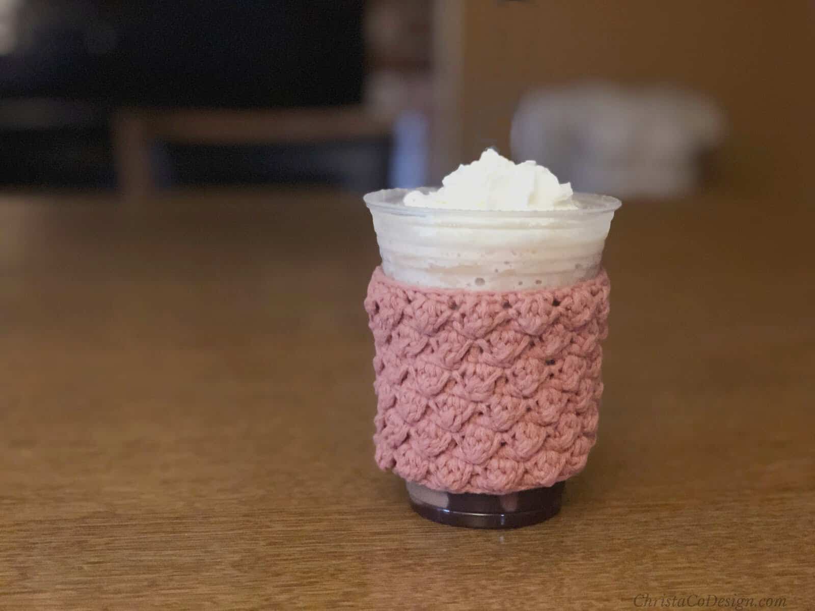 Cup on table with pink crochet sleeve.