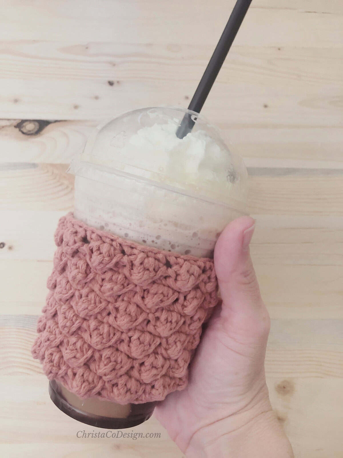 Hand holding cup with crochet sleeve in pink.