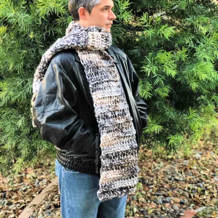 Man in black leather jacket in front of tree wrapped crochet super scarf.