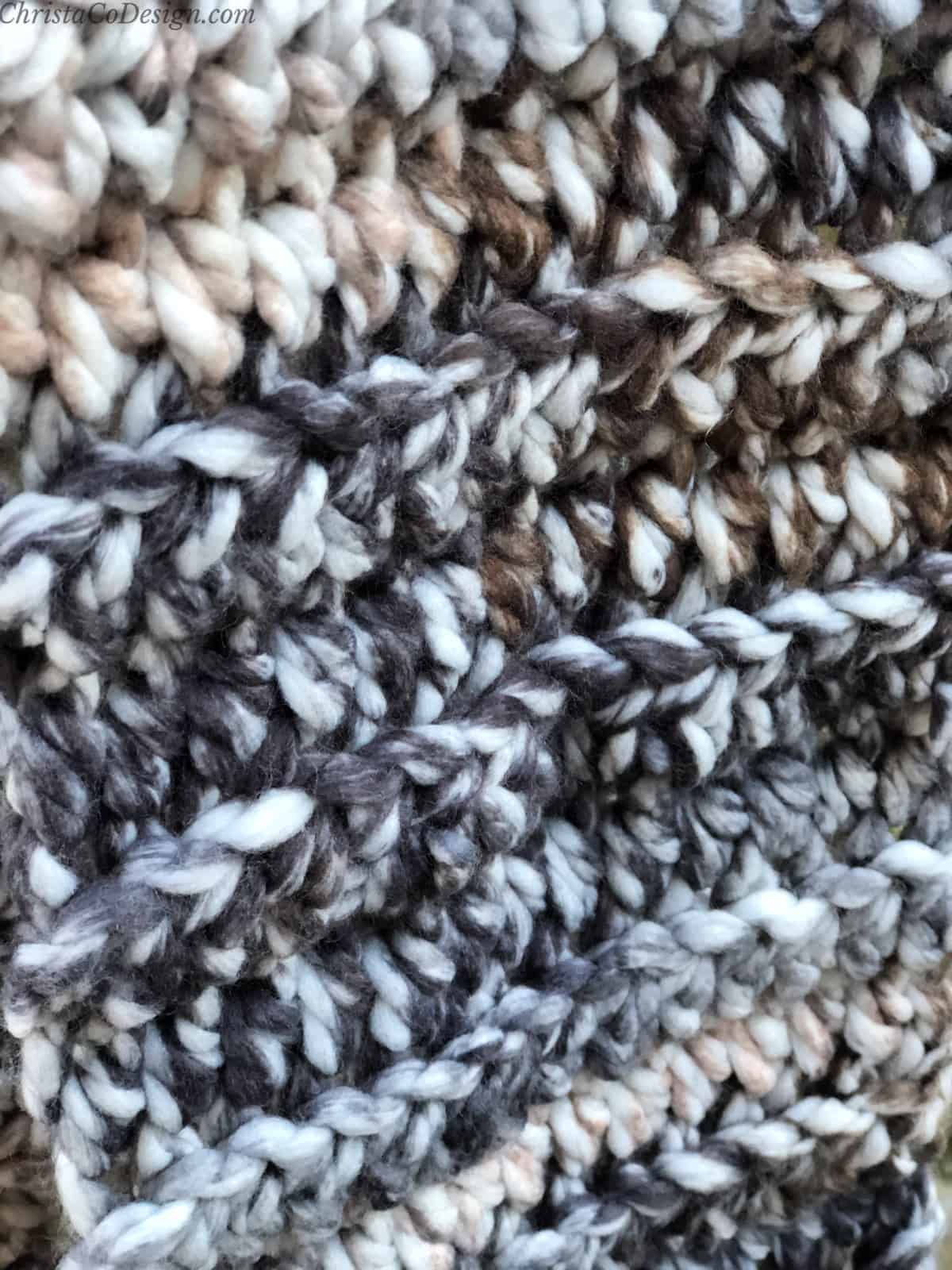 Close up of black, grey, brown and white stitches in crochet scarf.