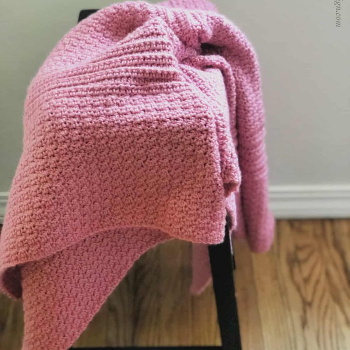 Pink crochet blanket draped on black stool.