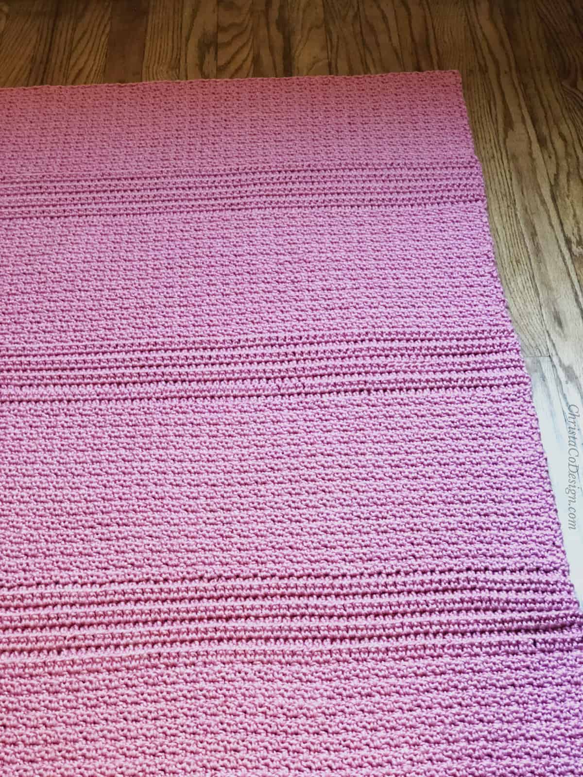 Pink crochet blanket laid flat on wood floor to show texture.