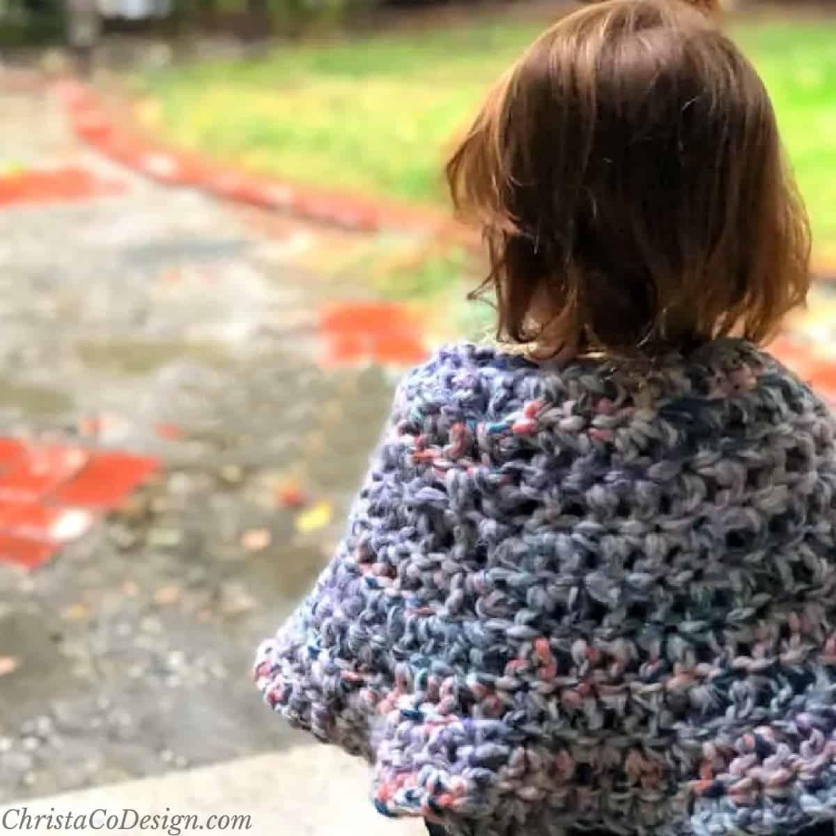 Toddler with colorful poncho looking out from front porch.