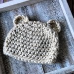 Cream crochet bear beanie flat on white square.