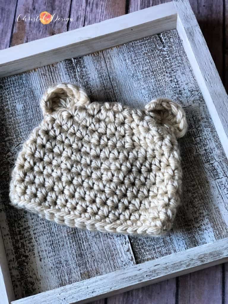 Cream crochet bear beanie flat on white square.