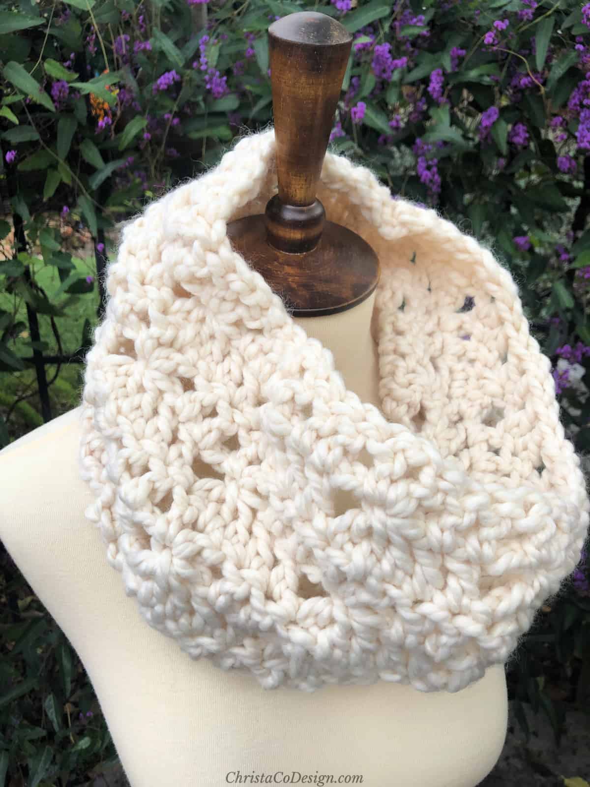 Cream crochet cowl with pretty stitches on mannequin outside.