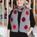 Woman in grey crochet scarf with red circles.