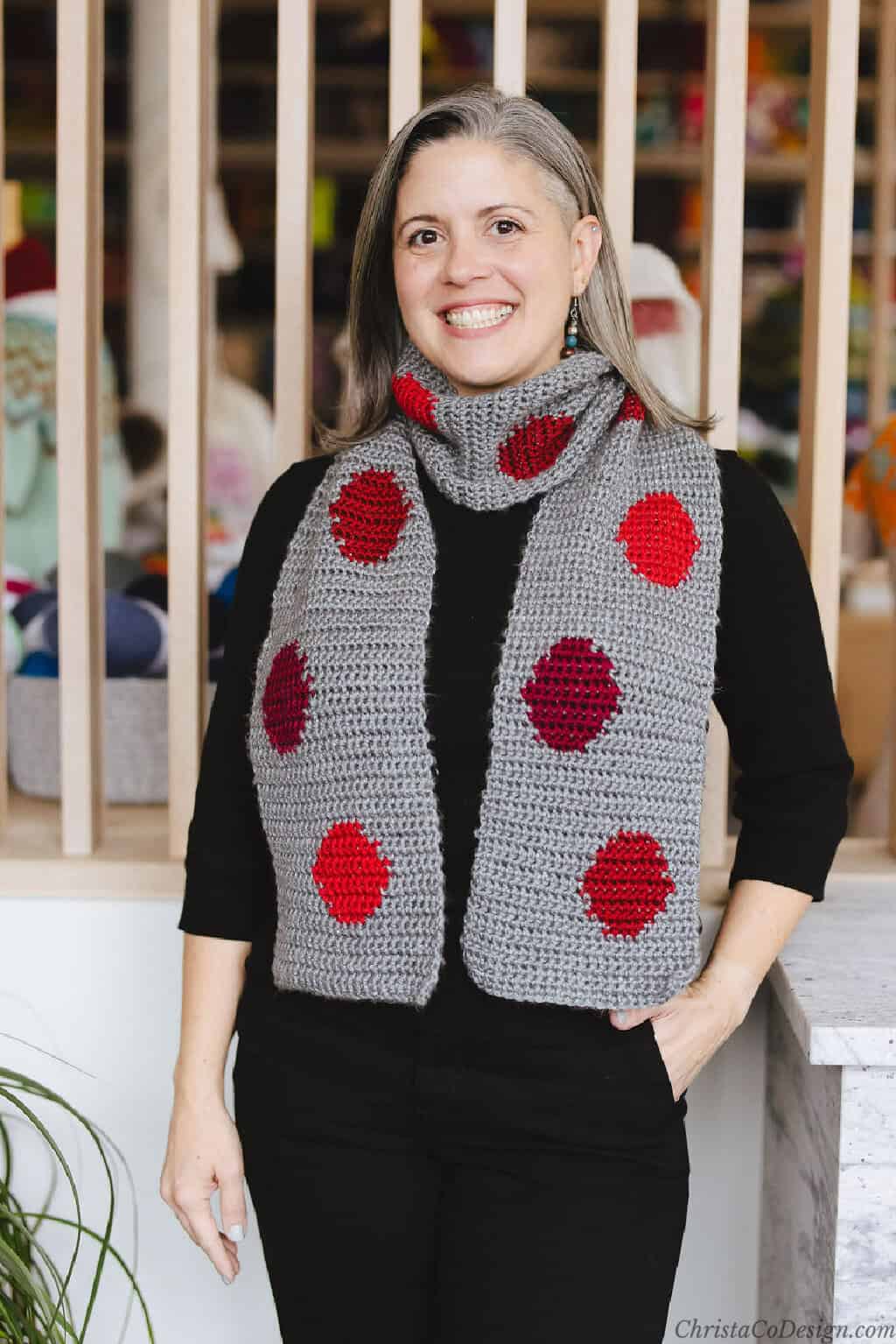 Woman in grey crochet scarf with red circles.
