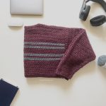 Mens simple striped crochet sweater in burgundy with grey stripes folded on table.