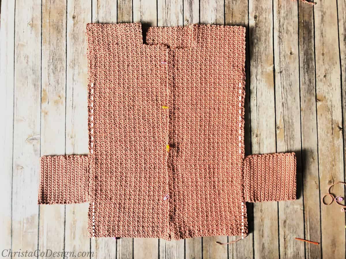 Pink crochet cardigan with pockets seamed on sides showing seam lines.