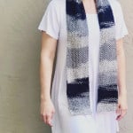 Woman with grey and black knit scarf draped over neck.