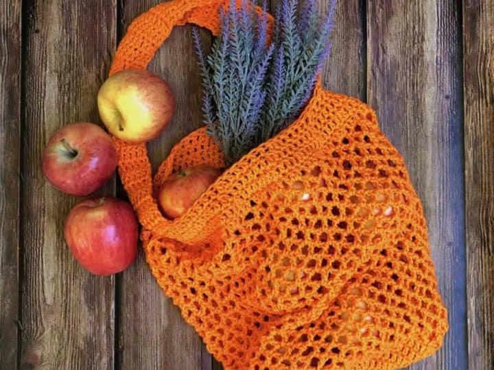 Free crochet market tote bag pattern in orange with apples and lavender on wood backdrop.