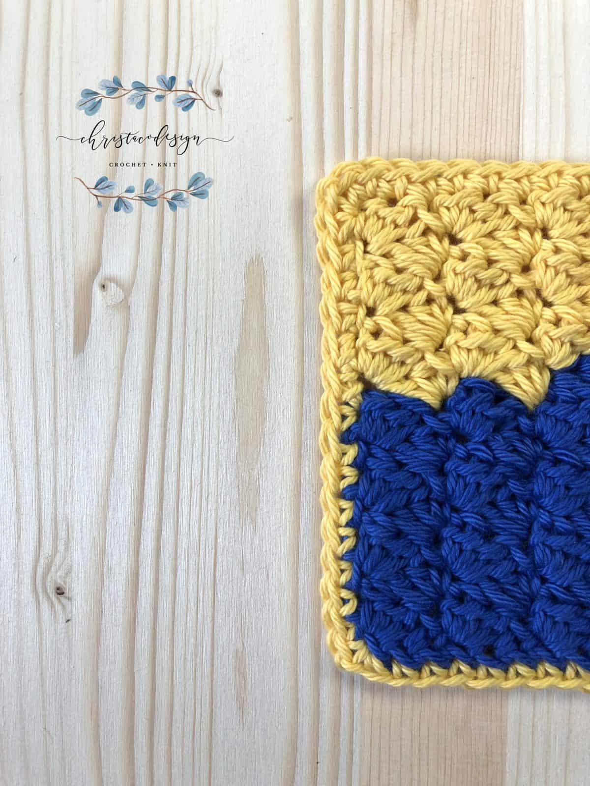 Yellow and blue crochet washcloth on wood table.