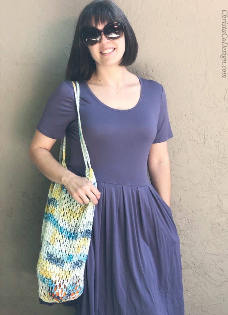 Woman in purple with crochet tote bag on shoulder.