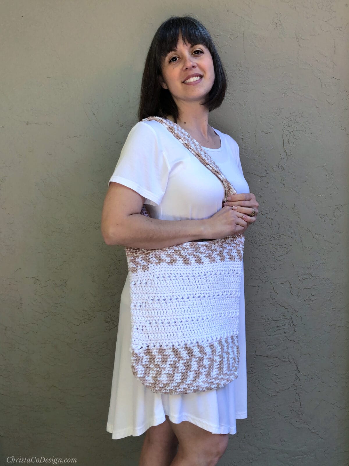 Woman in white with crochet bag on shoulder.