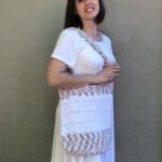 Woman in white with crochet bag on shoulder.