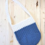 Blue and white crochet bag with long strap on wood table.