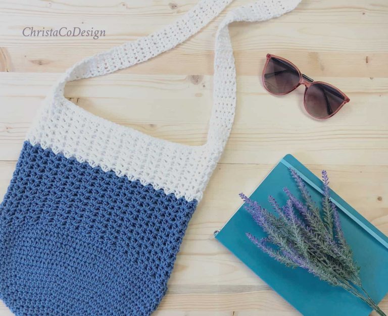 Blue and white free crochet tote bag with book and glasses on wood.