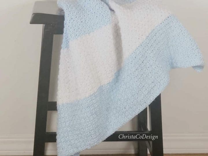 Crochet striped blue and white blanket on stool.