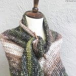 Crochet shawl in Lion Brand's Shawl in a Ball in greens and browns on mannequin secured with shawl stick.