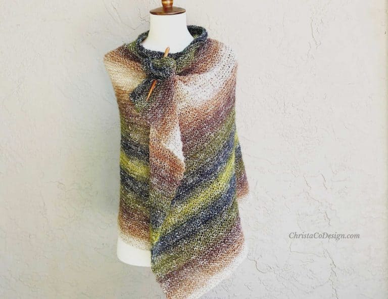 Green and brown knit shawl wrapped around mannequin in front of beige wall.