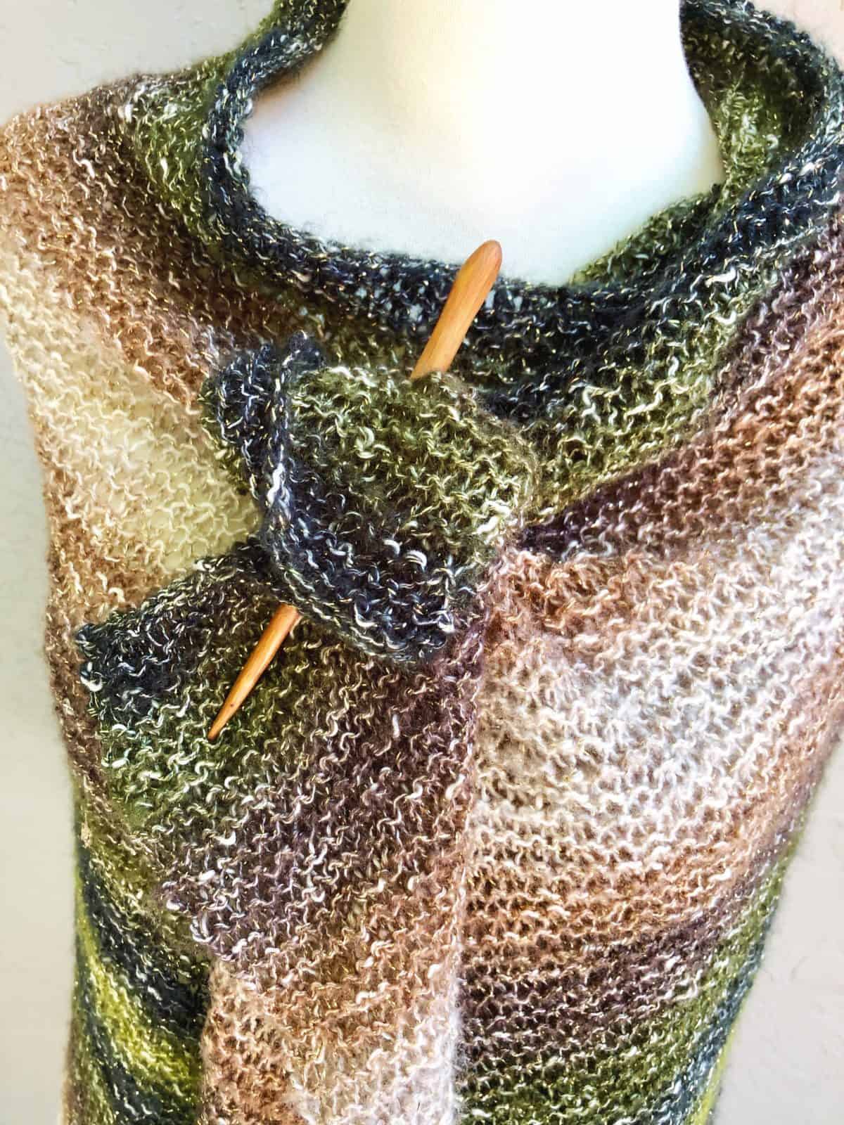 Close up on striped knit shawl secured with wood pin.