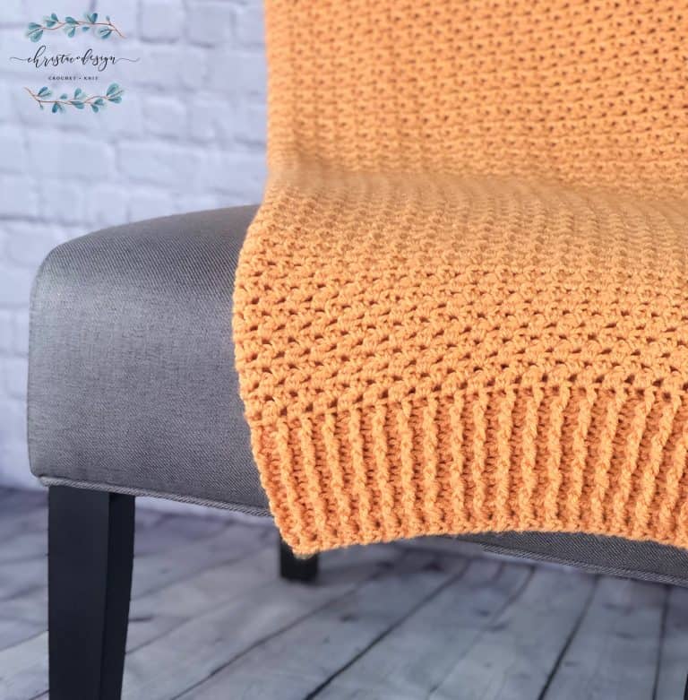 Orange crochet blanket with ribbed edging on grey chair.