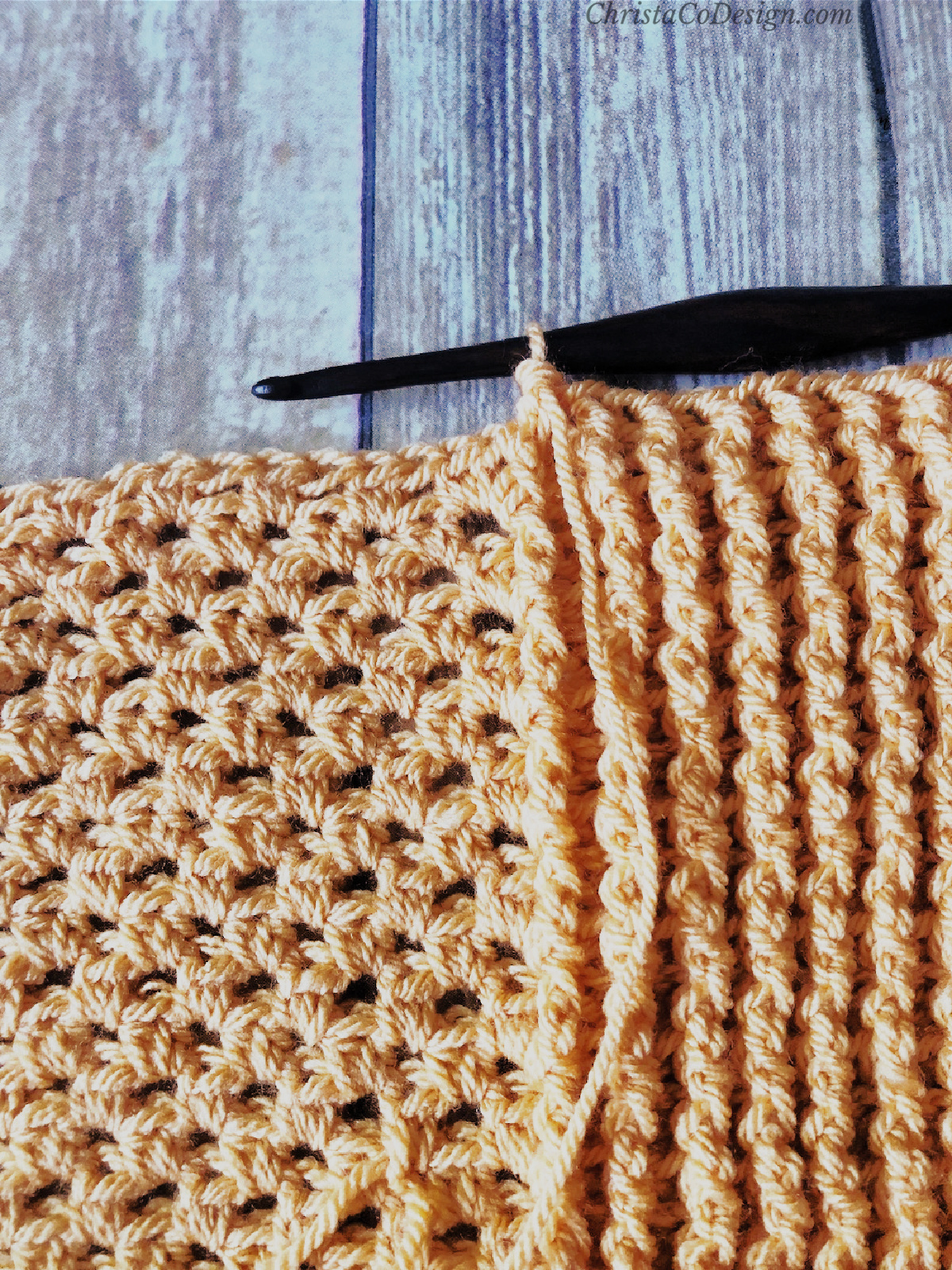 Crochet throw blanket in orange border stitches with hook.