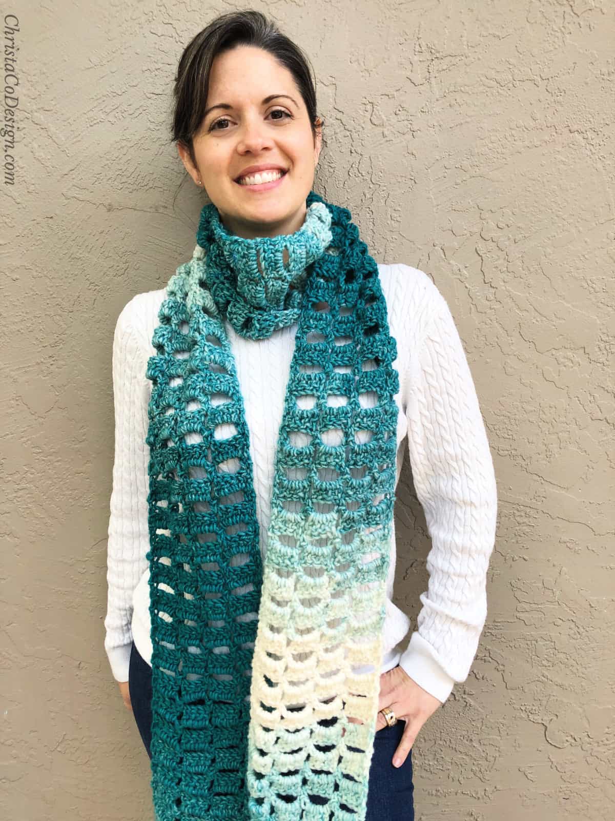 Woman smiling with ombre teal and cream crochet scarf on.